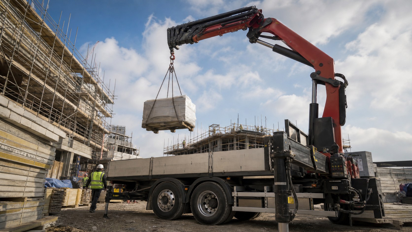 HIAB lorry-mounted crane lifting a pallet of materials from a flatbed truck on a construction site
