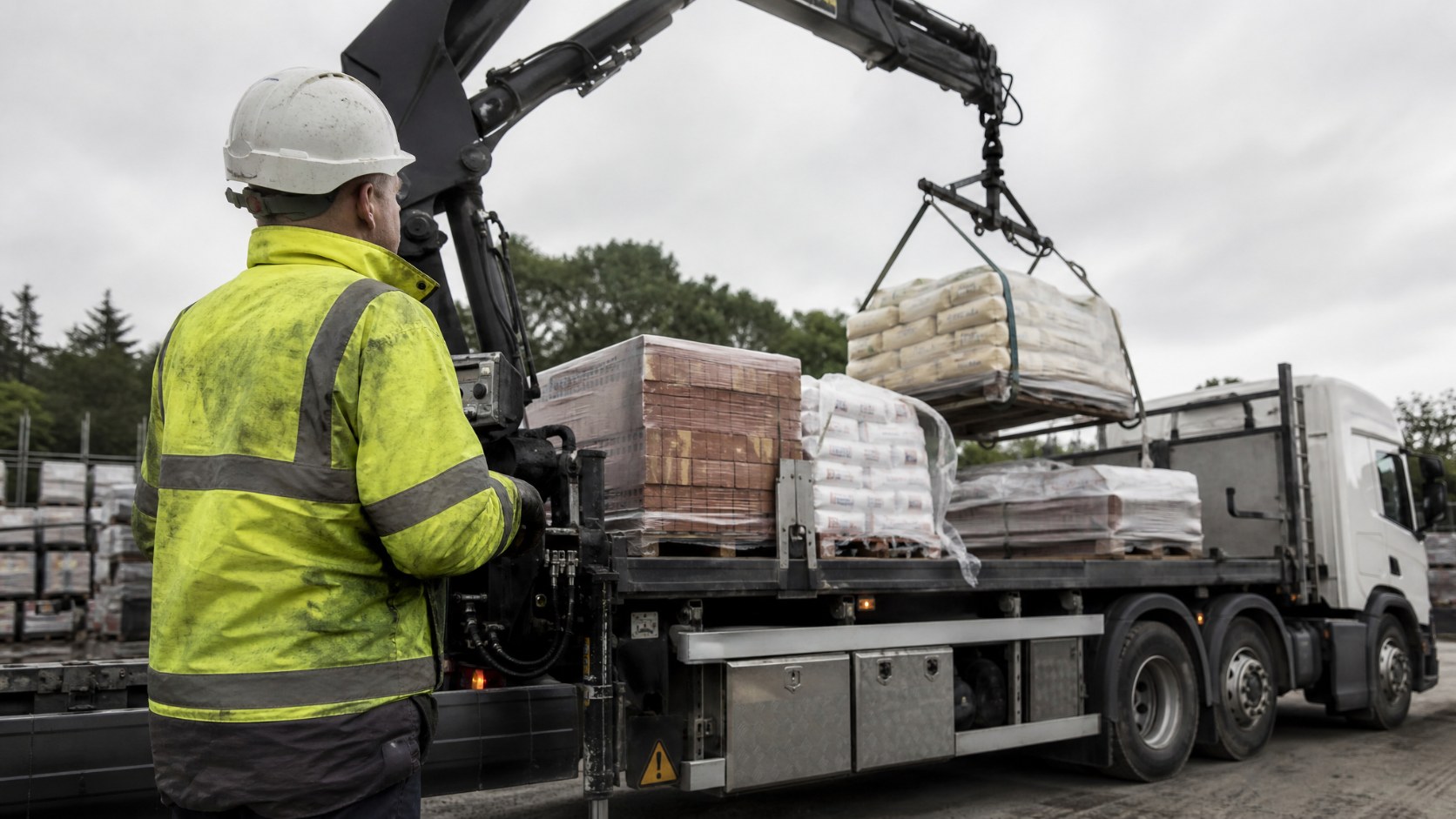 HGV driver operating a lorry-mounted HIAB crane to unload materials at a builders merchant yard