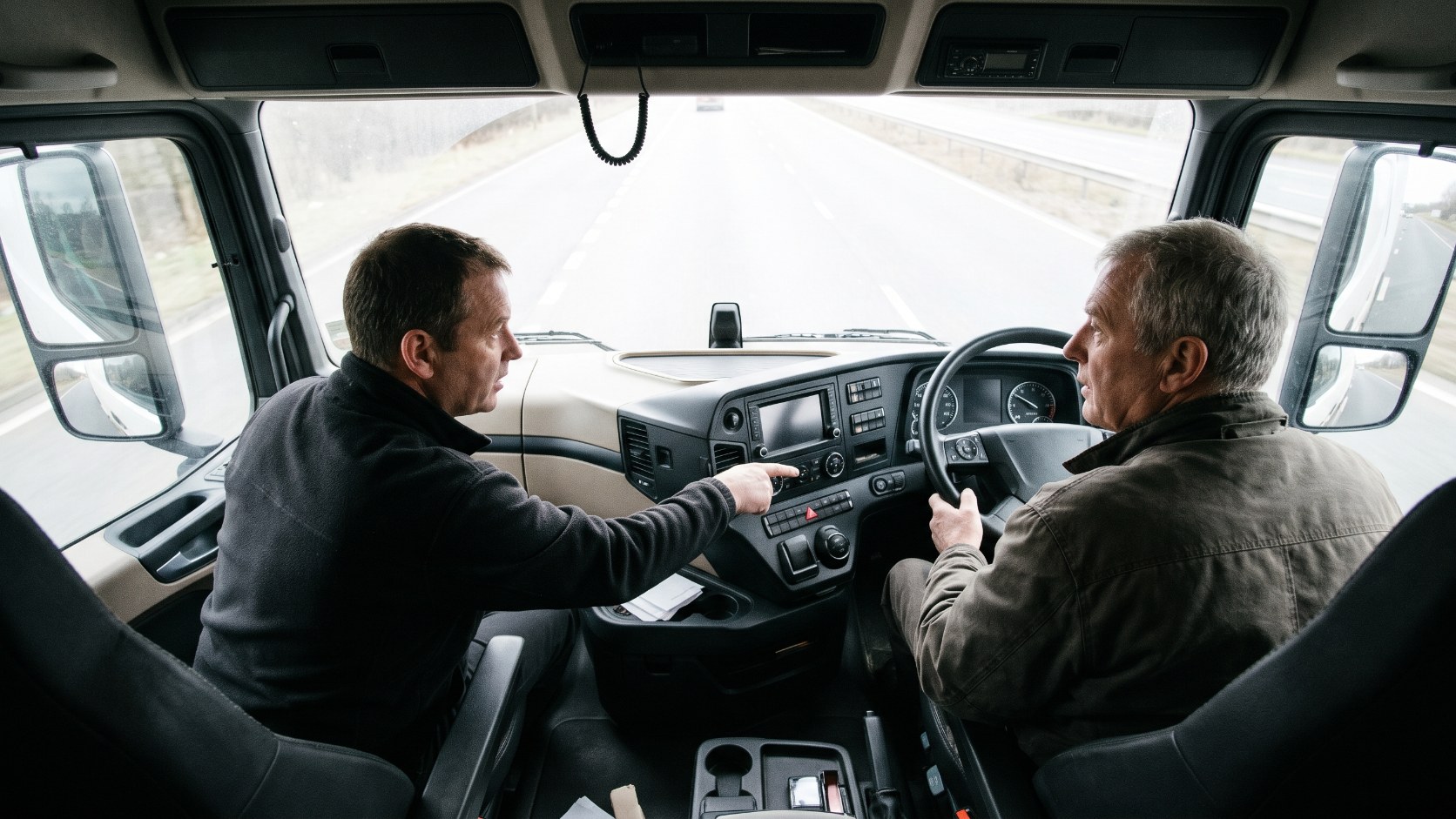 HGV driving instructor guiding a returning driver through refresher training in the cab