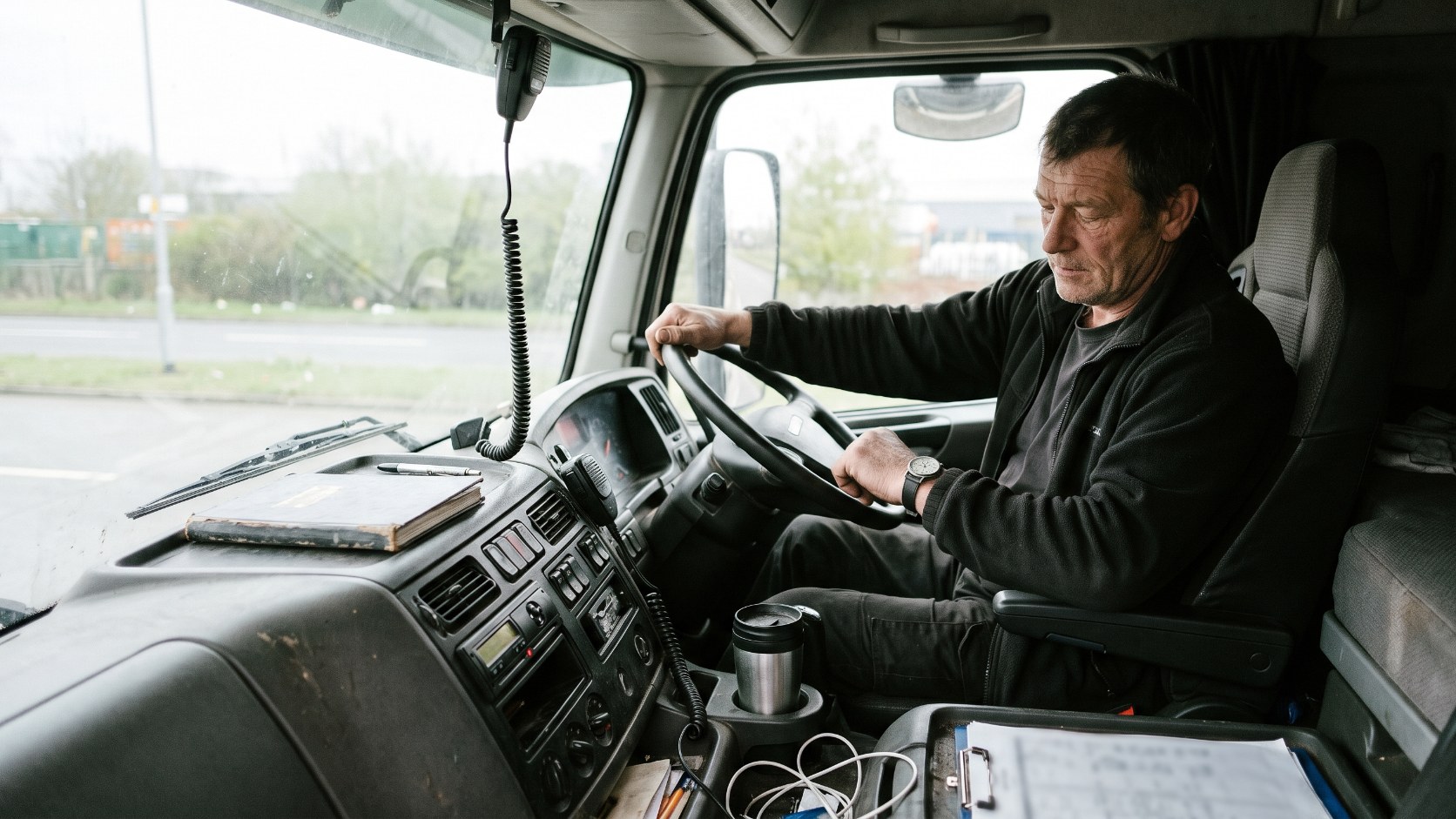 HGV driver checking the time against a paper logbook in the cab